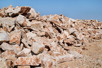 Brown Granite. Big pile of rocks for construction and boulders piled in a heap under a blue sky in summer time. A large pile of limestone in quarry. Pile of gravel and construction material.