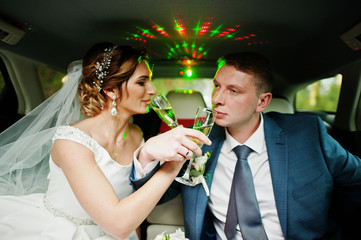 Newly married couple drinking champagne in the limousine on their wedding day.