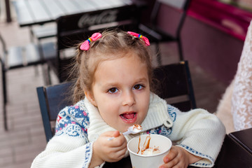 Little girl eating ice cream. Little girl emotionally eating In a cafe on the street