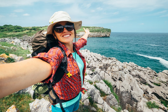 Happy woman backpacker traveler take a selfie photo on amazing ocean coast