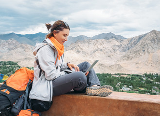 Backpacker with laptop sits on the top view point under mountain settelment