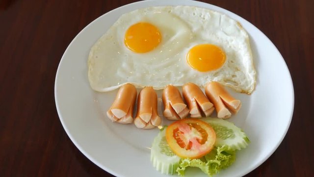 panning shot of fried eggs with sausages, tomatoes on wood table