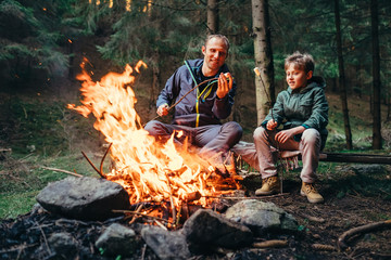 Father and son roast marshmallow on campfire - obrazy, fototapety, plakaty