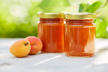 Apricot jam in glass jars with fresh fruit on a wooden table