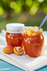 Apricot jam in glass jars with fresh fruit on a wooden table