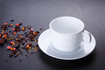 Tea cup with saucer on black background. Mixture herbal floral fruit tea with petals, dry berries and fruits.