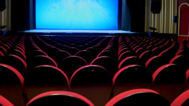 Camera motion behind the seats of an empty theater with background scene
