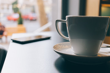 Cup of coffee and a mobile phone on a table in a cafe