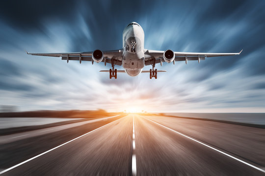 Fototapeta Airplane and road with motion blur effect at sunset. Landscape with passenger airplane is flying over the asphalt road and cloudy sky. Commercial plane is landing. Aircraft with blurred background 