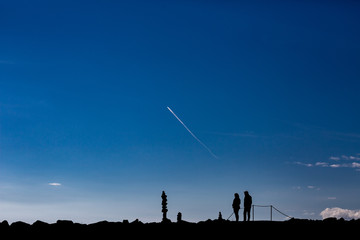 Silhouettes of adult couple under sky enjoying stone zen pile