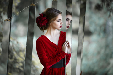 Mysterious girl in a long red dress watch mirrors in the nature. - obrazy, fototapety, plakaty