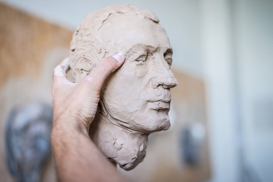 A sculptor sculpts a sculpture of a person's face. Horizontal frame