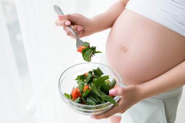 Pregnant woman starts to eat fresh salad in glass bowl. Healthy food, body and healthcare concept...