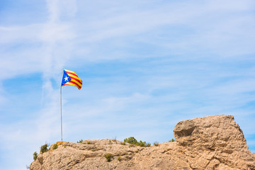 Fototapeta na wymiar The Spanish flag (Estelada) on the mountain, over blue sky background, Catalunya, Spain. Copy space for text.
