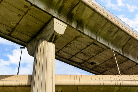 View from below of two highway junctions crossing one above the other, supported by a large concrete pillar.