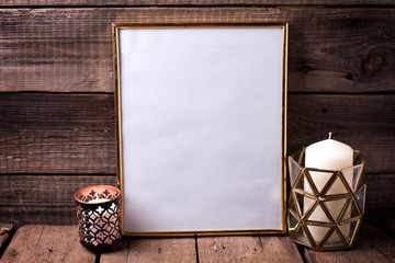 Empty golden frame and  candles  on  aged wooden background.