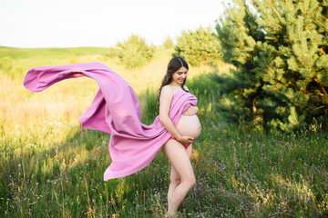 Pregnant woman in pink underwear in a wheat field in country nature on a beautiful sunny day