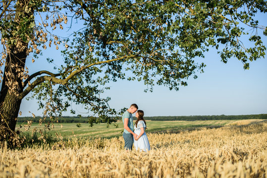 Romantic kissing Pregnant couple in a wheat field. Pregnant woman with her husband holding big belly with baby inside in nature on a beautiful sunny day