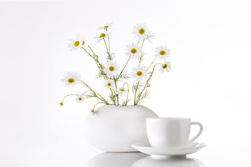 Bouquet of chamomiles flowers in a white vase and a cup on a white background