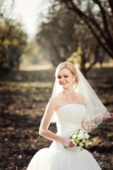 Fototapeta na wymiar Blonde bride in a white dress in a sunlit park