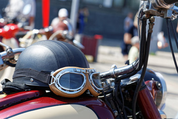 Black vintage moto helmet with glasses on motorcycle against blurred background