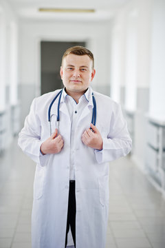 Handsome and confident young doctor in white coat with stethoscope posing in the hospital.