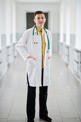 Fototapeta premium Handsome and confident young doctor in white coat with stethoscope posing in the hospital.
