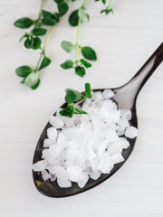 coarse sea salt in black spoon on white background with thyme. Copy space. Top view or flat lay.