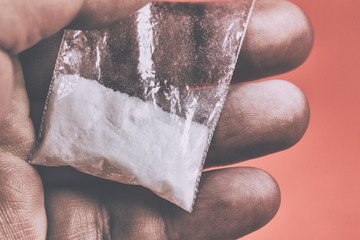 Mans hand holds plastic packet with cocaine powder or another drugs. Drug dealer