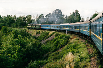 Photo of riding train among summer nature.  View out of window. Travelling by train.  Railroad turn. Going to vacation. Tourism and voyage.  Railway outdoor.  Vintage locomotive moving with old wagons