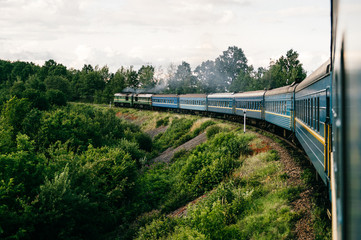Photo of riding train among summer nature.  View out of window. Travelling by train.  Railroad turn. Going to vacation. Tourism and voyage.  Railway outdoor.  Vintage locomotive moving with old wagons