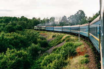 Photo of riding train among summer nature.  View out of window. Travelling by train.  Railroad turn. Going to vacation. Tourism and voyage.  Railway outdoor.  Vintage locomotive moving with old wagons
