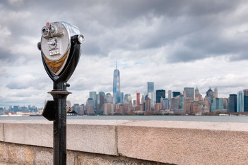 Fototapeta na wymiar Binoculars on Ellis Island pointed towards Manhattan's skyline in a cloudy day