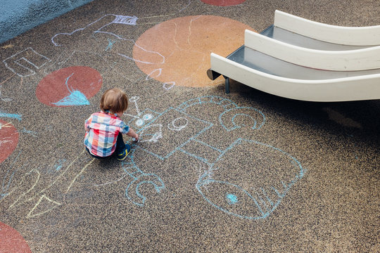 A young toddler at a playground drawing a chalk robot.