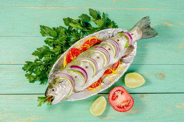 Raw fish trout cooked for cooking with lemon and tomatoes on a plate with foil. On a blue wooden...