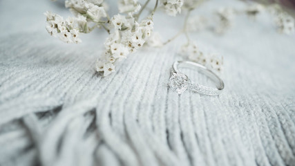 Close up of elegant diamond ring with white flower and gray scarf background. Wedding ring.