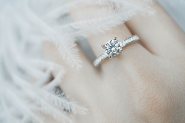 Close up of elegant diamond ring on the finger with feather and gray Scarf background. Diamond ring. - obrazy, fototapety, plakaty