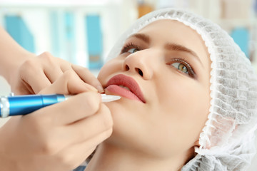 Young woman having permanent makeup on lips in beautician salon
