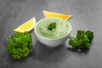 Delicious yogurt sauce in bowl with ingredients on grunge background
