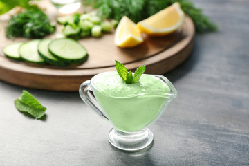 Delicious yogurt sauce in gravy boat with ingredients on grunge background