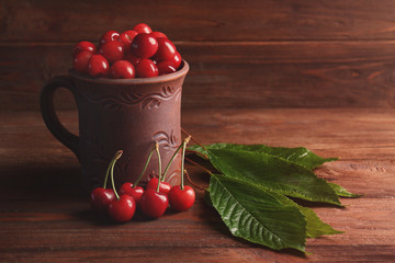 Mug with sweet cherries on wooden background