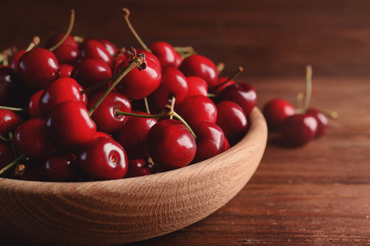 Bowl with sweet cherries on wooden background