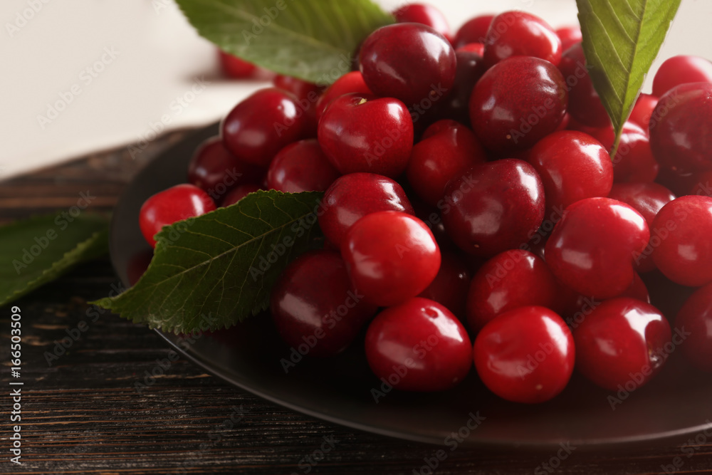 Wall mural Plate with sweet cherries with leaves on table, closeup