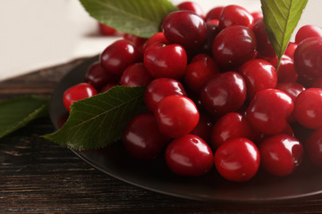 Plate with sweet cherries with leaves on table, closeup