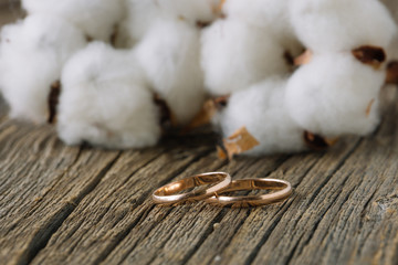 Wedding rings on wood with cotton flowers on background. Concept of rustic wedding