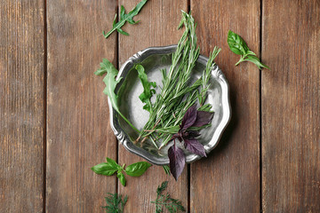 Metal plate with rosemary, basil and arugula on wooden background