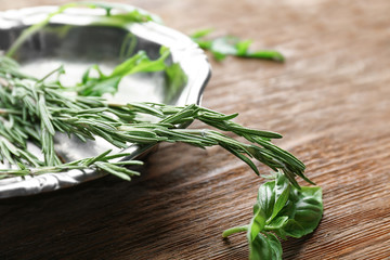 Metal plate with rosemary and basil on wooden table