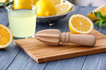 Cutting board with squeezer, glass of juice and lemons on wooden table