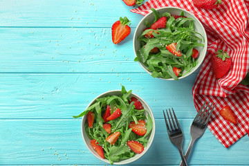 Bowls of salad with arugula leaves and strawberry on wooden background