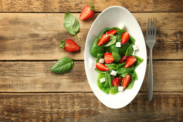 Plate with strawberry spinach salad on wooden background
